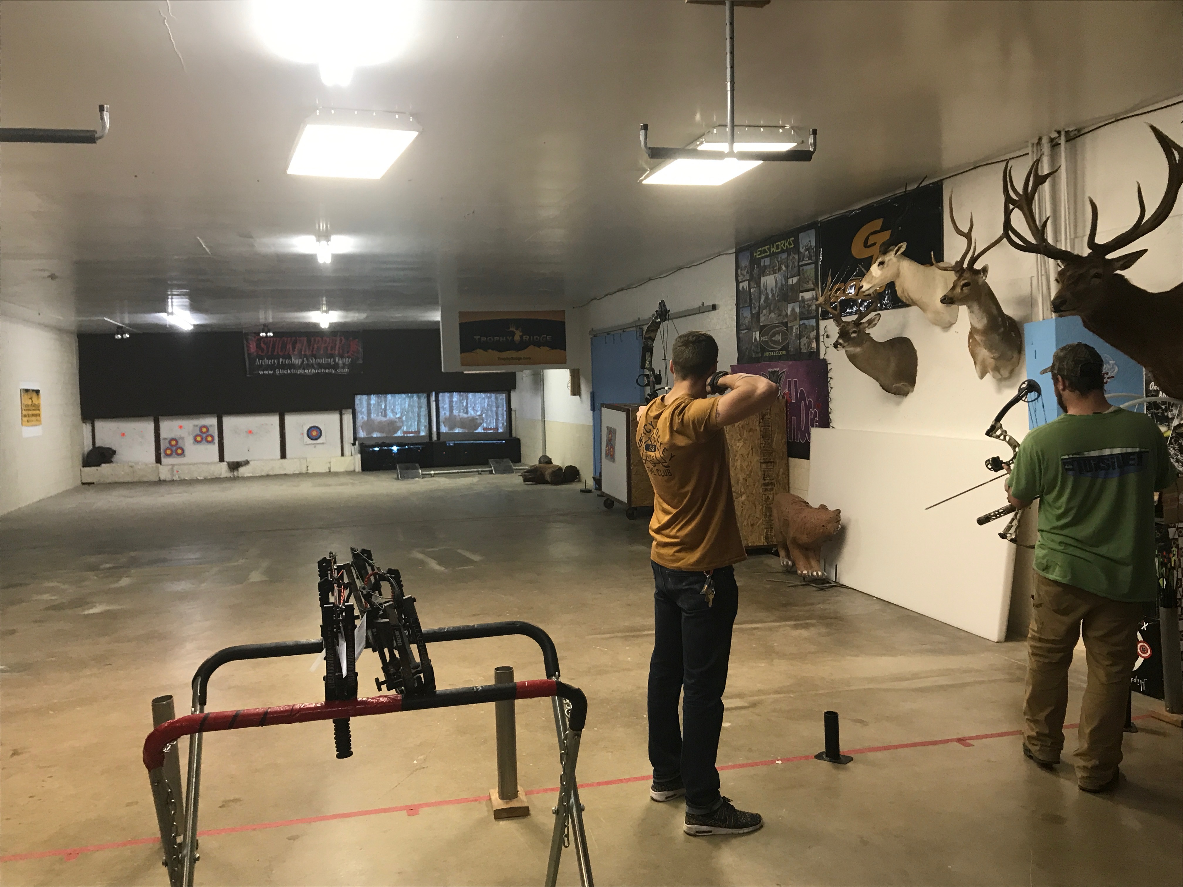 Inside the Stickflipper Archery range — shooters on the line with trophy mounts and 3D targets